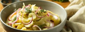 Eine Schale mit Kartoffel-Gurken-Salat und roten Zwiebeln.