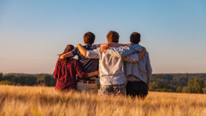 Vier junge Leute stehen mit dem Rücken zur Kamera in einem Feld und haben sich an den Schultern umarmt.