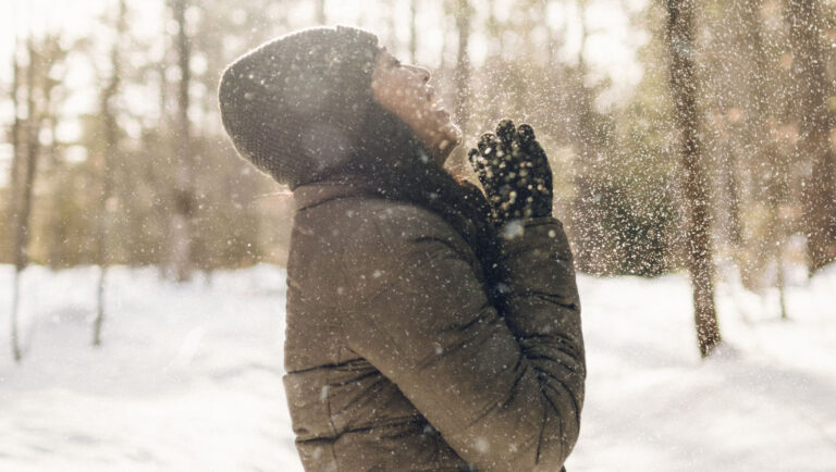 Junge Frau mit dickem Wintermantel steht im Schnee