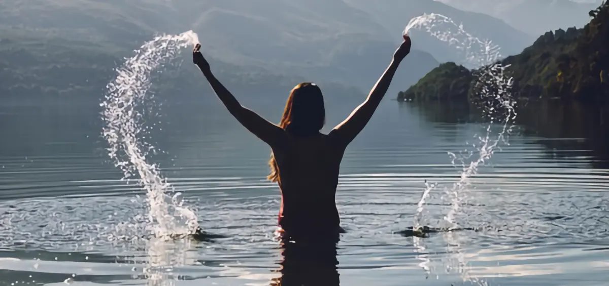 Eine Frau im See wirft das Wasser um sich herum beim Armen Hochheben.