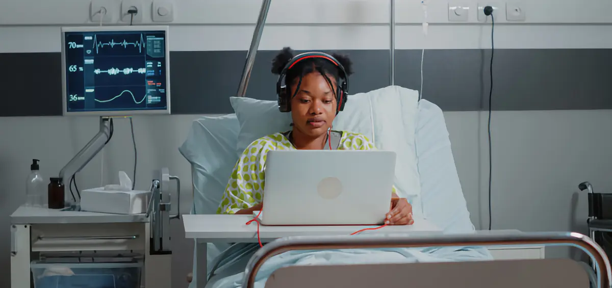 Eine Frau im Bett im Krankenhaus mit Kopfhörern arbeitet am Laptop