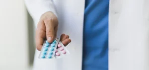 Ein Arzt im Kittel hält zwei Tablettenblister mit unterschiedlich gefärbten Tabletten.