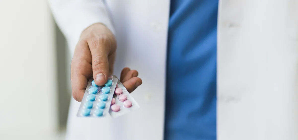 Ein Arzt im Kittel hält zwei Tablettenblister mit unterschiedlich gefärbten Tabletten