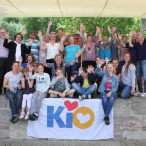 Eine Gruppe mit mehreren Familien posiert für die Kamera auf einer Steinmauer und sie halten jubelnd die Hände in die Luft