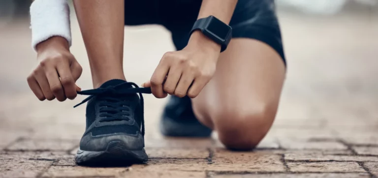 Eine junge Läuferin bindet sich kniend einen schwarzen Turnschuh zu.