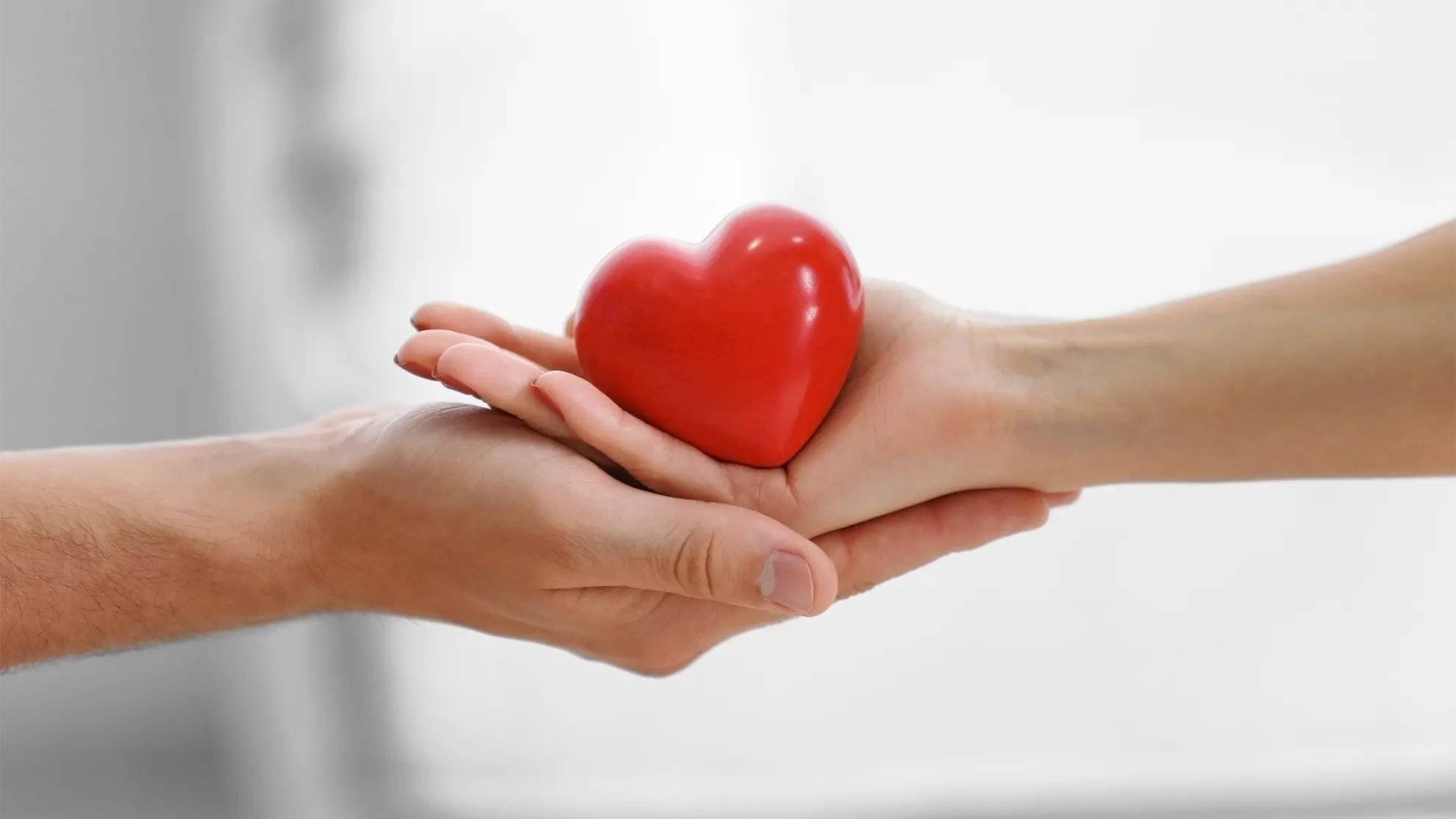 Eine Hand überreicht ein Objekt in Herzform einer anderen Hand.