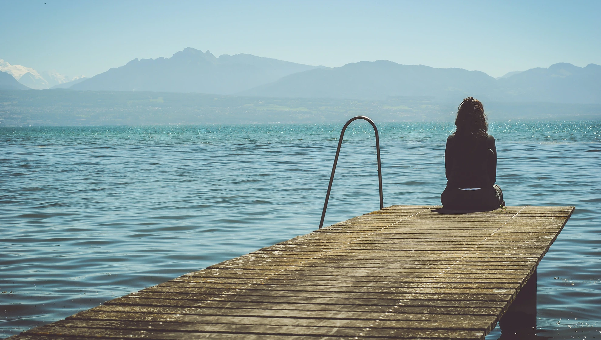 Junge Frau sitzt auf einem Pier und blickt aufs Meer