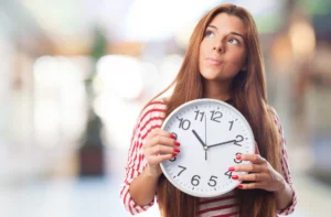 Eine junge Frau hält eine analoge Uhr in den Händen und blickt nach oben.