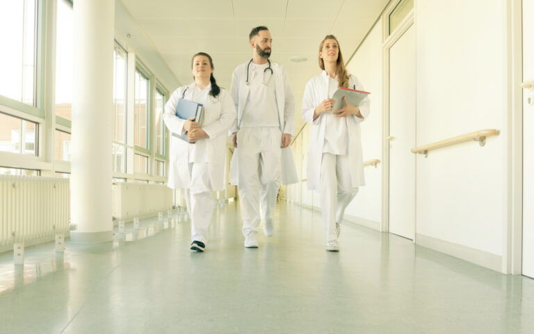 Ein Team aus zwei Ärztinnen und einem Arzt mit Patientenakten geht einen Gang im Transplantationszentrum entlang.