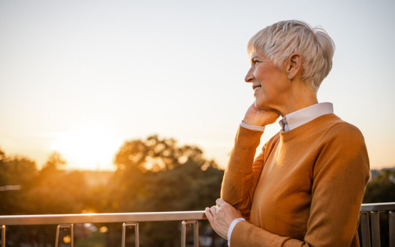 Die Aufnahme zeigt eine ältere Dame, die nach einer Nierentransplantation positiv und selbstbewusst in die Abendsonne blickt.