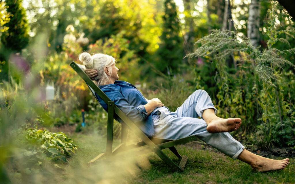 Frau mittlerettn Alters sitzt im Garten auf einem Liegestuhl und freut sich auf die Zeit nach der Transplantation