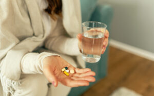 Eine Frau hält Tabletten in ihrer rechten Hand, in ihrer linken Hand hält sie Glas mit Wasser
